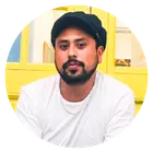 Man with beard wearing a black cap and white shirt sitting against a yellow background.